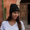 A person wearing a black beanie hat with an embroidered design on the front.
