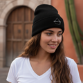 A person wearing a black beanie hat with an embroidered design on the front.