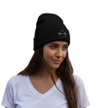 A woman wearing a black knit beanie with a small white embroidered Mexico City logo on the front, paired with a white V-neck t-shirt, set against a plain white background.