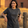 A woman wearing a black denim t-shirt with a graphic on the chest, standing against a white background.