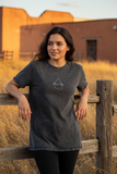 A woman wearing a black denim t-shirt with a graphic on the chest, standing against a white background.