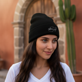A woman wearing a black beanie hat with an embroidered design on the cuff.