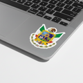 A die cut bubble-free sticker featuring the official coat of arms of Queretaro, predominantly white in color. Applied next to the trackpad of a Macbook Pro.