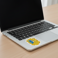 Sticker with the Official Coat of Arms of San Luis Potosi, featuring a yellow shield with a blue background, a figure, and a mountain. Next to the trackpad of a MacBook Pro.