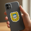 A hand holding a dark gray smartphone case with a yellow and white embroidered-style crest sticker on the back, shown against a softly blurred indoor background.