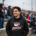 A man smiling in a stadium wearing a black hoodie with a red and white 'Piratas de Campeche' logo on the front, with blurred bleachers and spectators in the background.