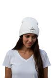 A woman wearing a white knit beanie with a black embroidered logo that reads 'The Philosopher' and a small fish icon, paired with a white V-neck t-shirt against a plain white background.