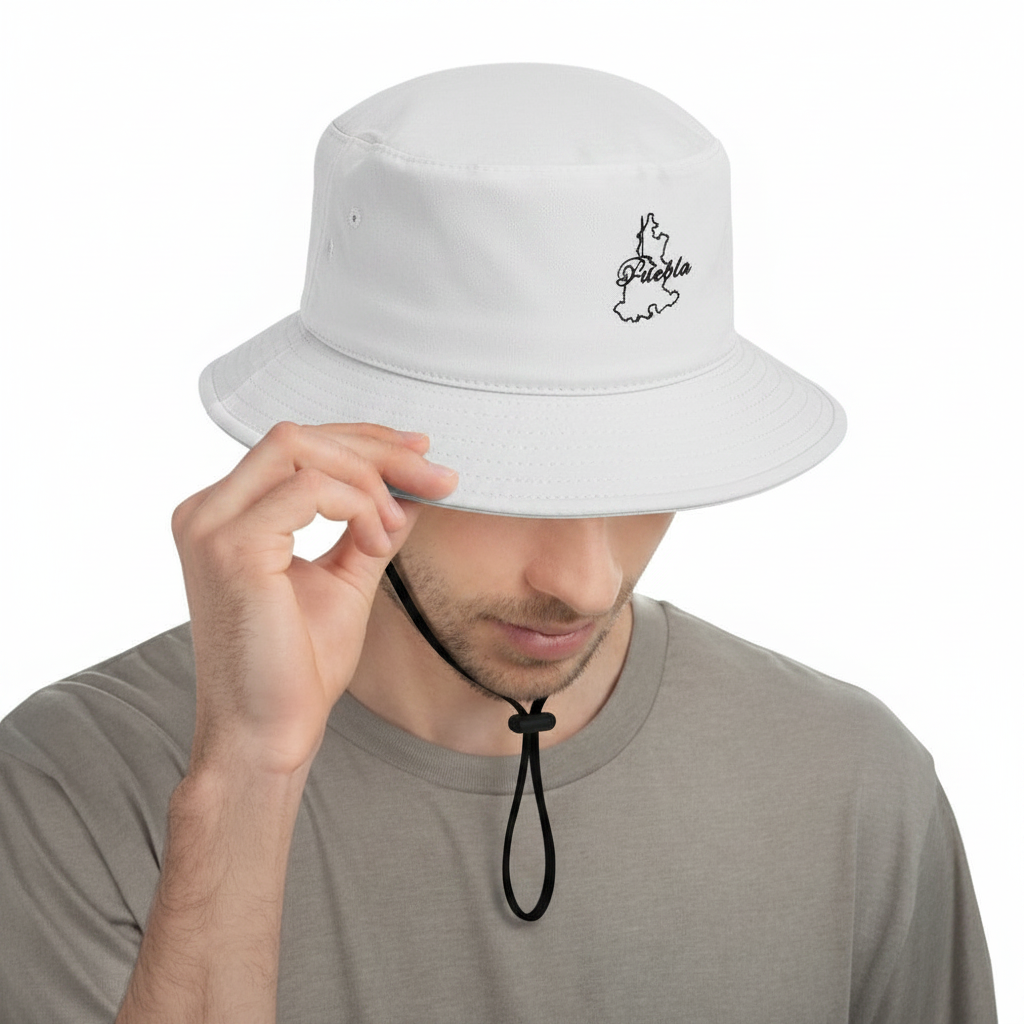 A man wearing a white Puebla bucket hat with a small black embroidered logo on the side, holding the brim with one hand. The background is solid white.