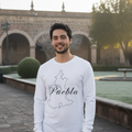 A man wearing a white long-sleeve t-shirt with a black outline map of Puebla and the word 'Puebla' written in script, standing outdoors in front of a stone archway and greenery.