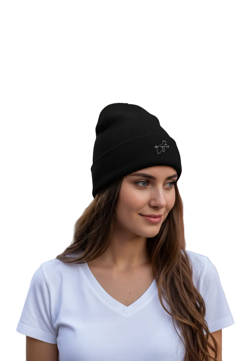 A woman with long brown hair wearing a black knit beanie with a small white embroidered Quintana Roo logo, paired with a white V-neck t-shirt, set against a solid white background.