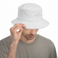 A man wearing a white Quintana Roo bucket hat with a small gray embroidered logo on the side, holding the brim with one hand against a plain white background.