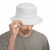 A man wearing a white Quintana Roo bucket hat with a small gray embroidered logo on the side, holding the brim with one hand against a plain white background.