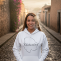 A person wearing a white unisex hoodie with a graphic of the Chihuahua state map in black.