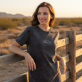 A woman wearing a short-sleeved black denim t-shirt with a round neckline and machine washable label on the bottom front.