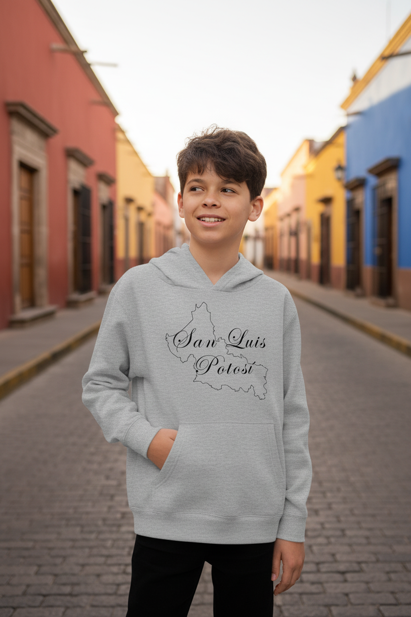 A smiling young boy stands on a cobblestone street wearing a light gray hoodie with a black outline map of Colombia and the text 'San Luis Polot' printed on the front. The background shows colorful colonial-style buildings in a street scene.