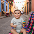 A baby wearing a short sleeve gray bodysuit with 'San Luis Potosi' text on it.