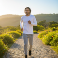 A man jogging on a cobblestone path outdoors during golden hour, wearing a white long-sleeve athletic shirt and light gray jogger pants.