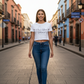 A woman walking down a cobblestone street wearing a white graphic crop top and blue jeans.