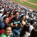 A man in a crowded stadium seat wearing a black t-shirt with 'Saraperos' written in teal script, smiling and gesturing excitedly. The background shows a packed baseball stadium with fans and the field.