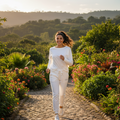 A woman jogging on a cobblestone path in a lush garden, wearing a matching white long-sleeve top and jogger pants set.
