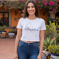 A woman stands outdoors in a courtyard wearing a white cropped T-shirt with a black outline of the state of Sinaloa and the word 'Sinaloa' printed across the chest, paired with blue jeans.