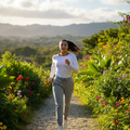 A woman jogging on a cobblestone path surrounded by lush green garden plants and colorful flowers under a bright sky with distant mountains.