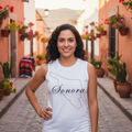 A woman stands on a cobblestone street wearing a white sleeveless tank top with a black outline of the state of Sonora and the word 'Sonora' across the front, paired with black pants.