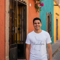 A smiling man wearing a white graphic t-shirt with a black outline of Panama and the word 'Tamaulipas' stands on a cobblestone street in front of a colorful building with orange, teal, and yellow walls.