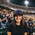A smiling woman in a Tigres de Quintana Roo baseball stadium wearing a navy blue cap and a black t-shirt, with a cheering crowd in the background.