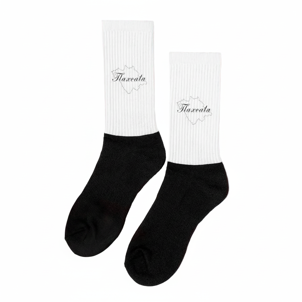 A pair of black and white Tlaxcala socks displayed upright on a surface with dried lavender surrounding them. The socks have the word 'Tlaxcala' written on the white cuff.