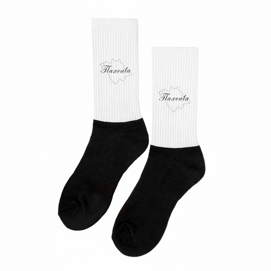 A pair of black and white Tlaxcala socks displayed upright on a surface with dried lavender surrounding them. The socks have the word 'Tlaxcala' written on the white cuff.