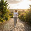 A woman jogging on a sunlit cobblestone path surrounded by lush green garden plants and trees.
