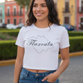 A woman wearing a white short-sleeved crop t-shirt with the word 'Tlaxcala' printed in black script on the front, paired with blue jeans.