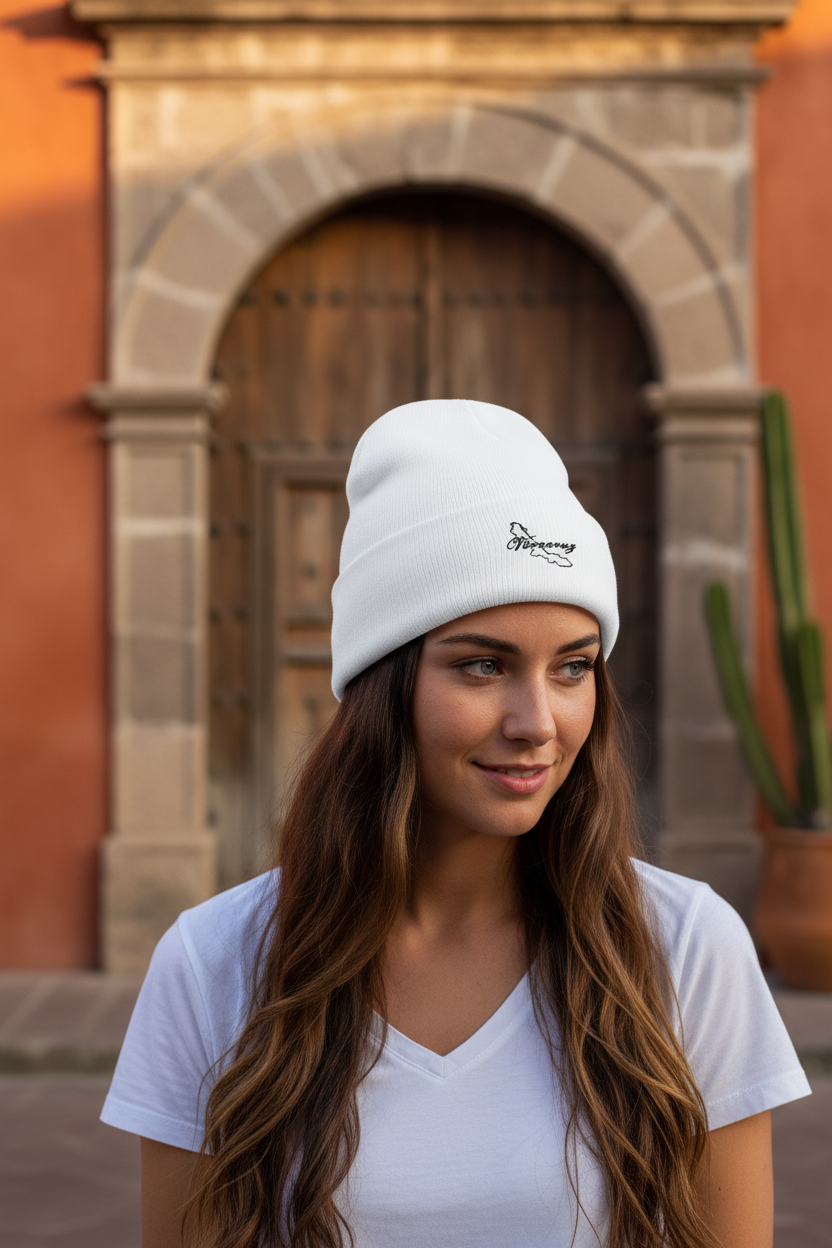 A woman with long brown hair wearing a white Veracruz embroidered beanie with a small black embroidered logo, standing in front of a warm-toned stone archway and wooden door.