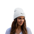 A woman with long brown hair wearing a white knit beanie with a small black embroidered logo on the front, paired with a white t-shirt, set against a solid white background.