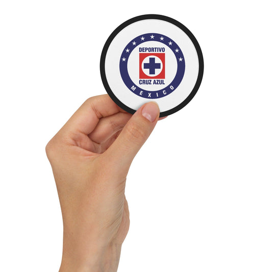 A hand holding a round embroidered patch with a white background and the text 'Cruz Azul' and 'MEXICO' on it.
