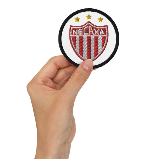 A hand holding a round embroidered patch with the text NECAXA and stars, predominantly white in color.