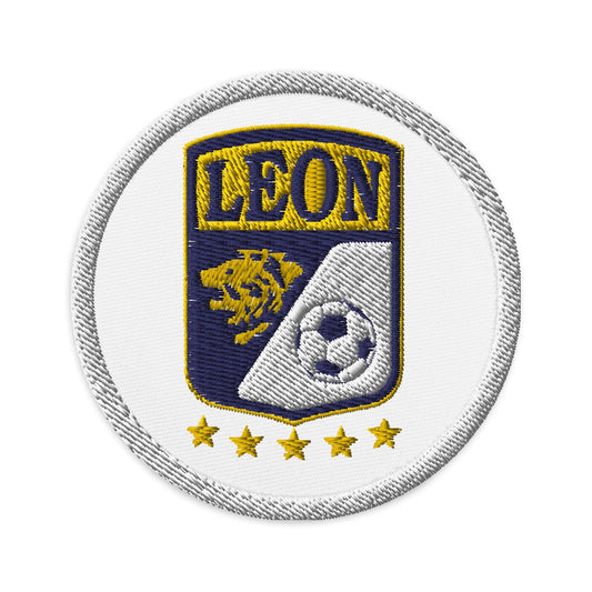 A round white embroidered patch with the text 'LEON' prominently displayed, featuring a gold lion and a soccer ball, with yellow stars on the side.