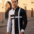 A man wearing a long-sleeve button-up shirt with a bold black and white geometric cross pattern, standing on a cobblestone street in front of a warm-toned building.