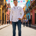 A man wearing a white long-sleeve western-style shirt with silver embroidery on the chest, blue jeans, and brown boots, standing on a colorful cobblestone street lined with vibrant buildings.