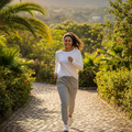 A woman jogging on a cobblestone path surrounded by lush green tropical plants and hills under warm sunlight.