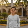 A child wearing a long sleeve white t-shirt with the text 'Yucatan' printed on the front.