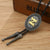 Black bolo tie with oval silver pendant and gold monogram, braided cord ends with beads