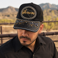 A Mexican model wearing a black Sonora charro-style hat in a desert vaquero setting. The embroidered Sonora name and map design are clearly visible on the front.