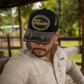 A Mexican model wearing a black Tabasco charro-style hat at a tropical Mexican ranch with lush green vegetation. The embroidered Tabasco name and map design are clearly visible on the front.